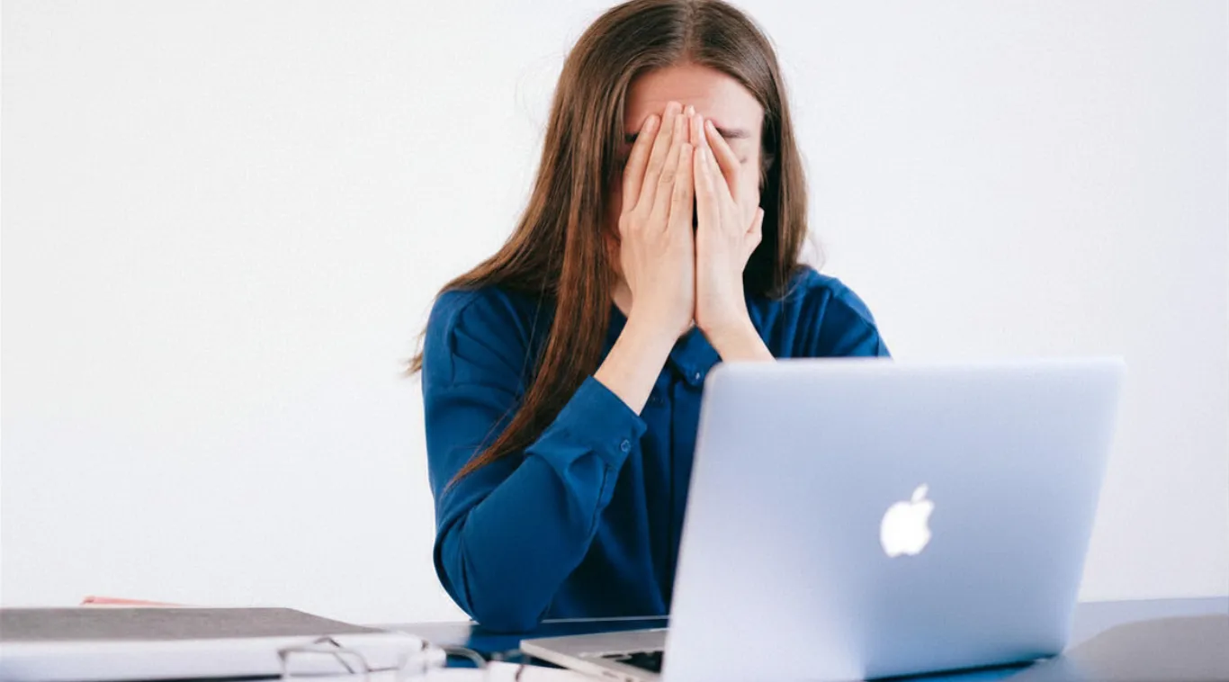 Woman covering her face while sitting at a laptop