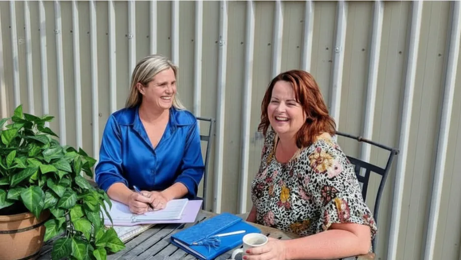 Two women smiling and talking over notebooks and coffee