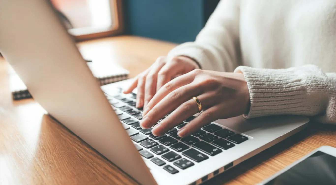 Hands typing on a laptop at a wooden desk